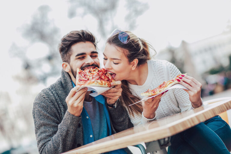 Couple eating pizza snack outdoors. They are sharing pizza and eating.