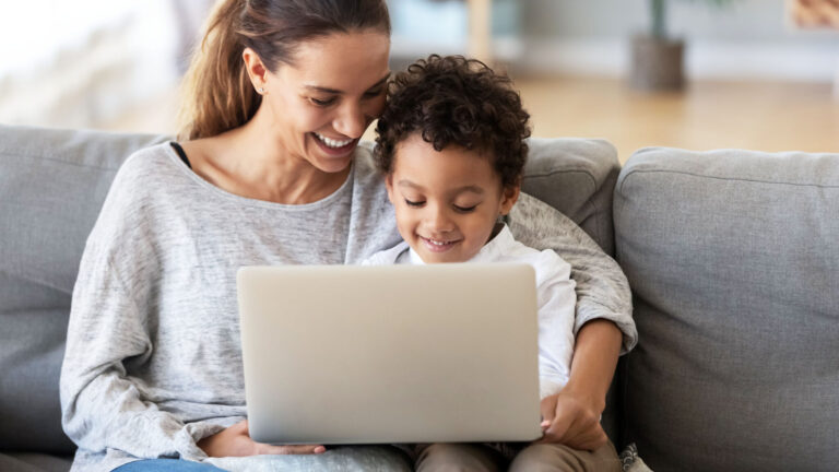 Smiling mother with African American son using laptop close up, happy mum and preschool child sitting on sofa at home, watching cartoons online or play video game, family having fun
