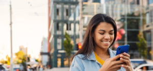 Young woman using her smartphone in a city center to compare mmf vs mma financial options.