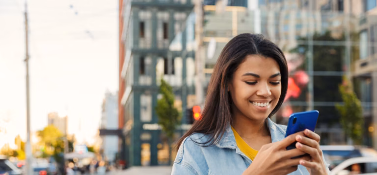 Young woman using her smartphone in a city center to compare mmf vs mma financial options.